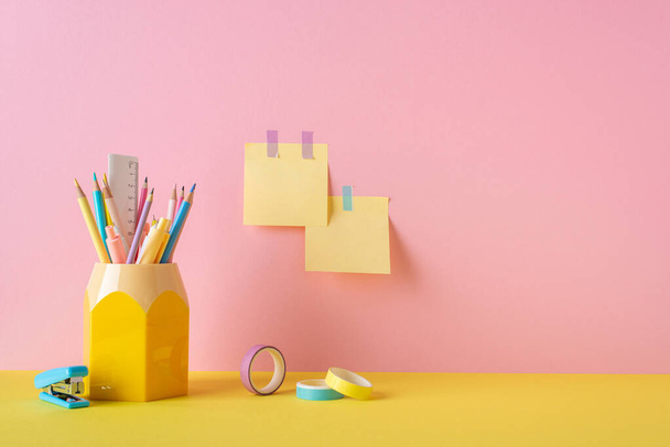 Back to school concept. Photo of school supplies adhesive tape pencil holder mini stapler and sticky note paper attached to pink wall - Foto, imagen
