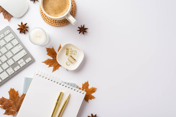 Autumn business concept. Top view photo of keyboard computer mouse notepad gold pen candle cup of coffee rattan serving mat binder clips yellow maple leaves and anise on isolated white background - 写真・画像