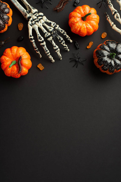 Top view photo of halloween decorations skeleton hands pumpkins candies centipedes and spiders on isolated black background with blank space - Photo, image
