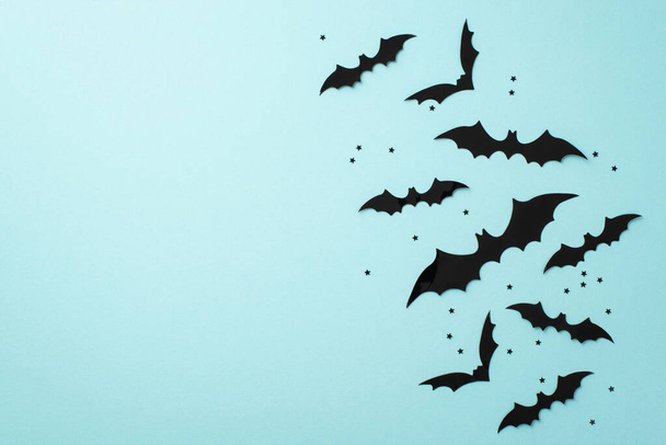 Концепция Хэллоуина. Фото силуэтов летучих мышей и черных конфетти на изолированном пастельно-голубом фоне с копирайтом - Фото, изображение