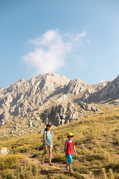 mother with a child on a hike walk along the road against the backdrop of mountains and blue sky. hiking and family vacations. family values - 写真・画像