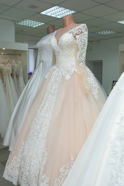 A beautiful cream wedding dress on a mannequin. A wedding dress on the background of other wedding dresses in a wedding salon. - Foto, Bild