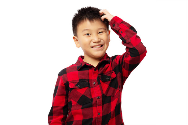 Μπερδεμένο παιδί ξύνει το κεφάλι φορώντας κόκκινο πουκάμισο απομονωμένο σε λευκό φόντο - Φωτογραφία, εικόνα