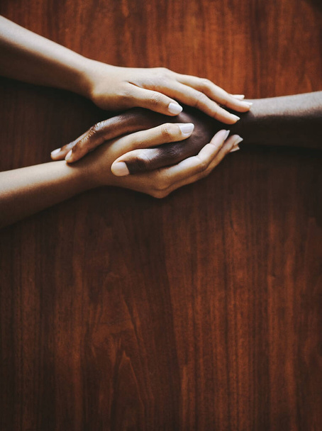 Support, love and a couple holding hands at a table from above with copyspace. Interracial friends praying, consoling and showing care at therapy or after bad news. Unity and affection after grief - Foto, Imagen