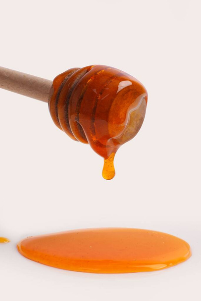 A vertical closeup of honey dripping from a wooden spoon on a white background - Photo, Image