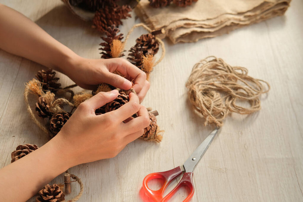 Part of a woman's hands making wall hangings from pinecones and jute rope - Foto, imagen
