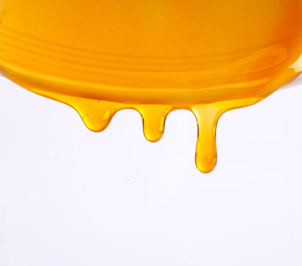 A closeup of honey dripping on a white background - Fotó, kép