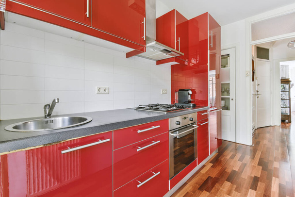 Fragment of interior of light narrow home kitchen with minimalist style red furniture with sink and stove - Foto, Imagem