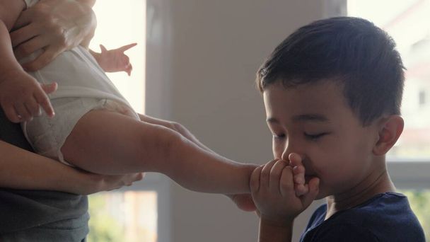 Cute preschooler kiss his baby brothers legs. High quality 4k footage - Foto, afbeelding
