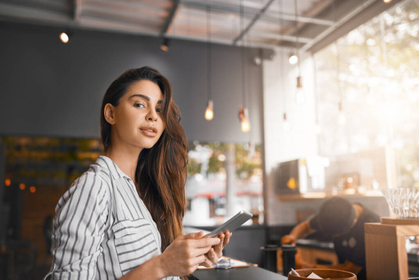 This tablet helps me keep things running smoothly. Cropped portrait of an attractive young woman working on a digital tablet while standing in her coffee shop - 写真・画像