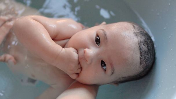Top view of Cute baby having bath. Mother holds and bathes baby. High quality 4k footage - Foto, Imagem