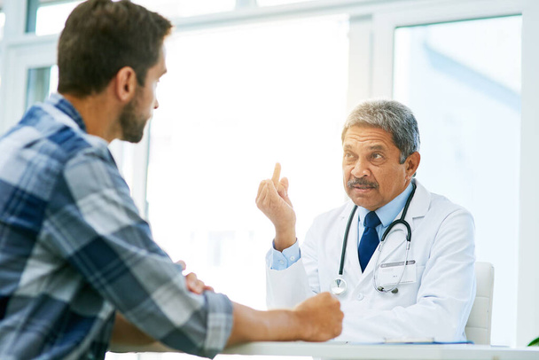 Theres one little issue that I need to bring to your attention. a confident mature male doctor consulting with a patient inside of his office during the day - Foto, immagini