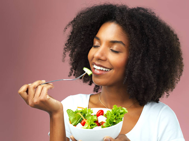 Λατρεύω το πόσο υγιές είναι. Στιγμιότυπο από μια ελκυστική νεαρή γυναίκα που τρώει σαλάτα σε ροζ φόντο - Φωτογραφία, εικόνα
