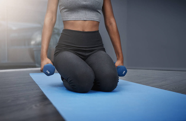 The end goal is worth every sacrifice. an unrecognizable young woman on her knees holding dumbbells while exercising on her gym mat at home - Fotó, kép