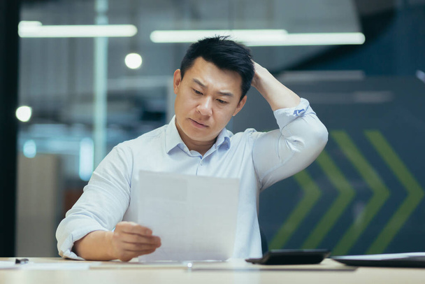 Stressed businessman holding face with his hands because having trouble. Bankrupt Asian Male is sitting with laptop computer and paperwork on desk at workplace in office. Business Mistake Financial. - 写真・画像