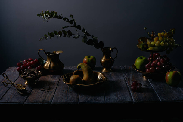 Fruit still life with grapes, apples, pears, chocolate and antique copper utensils on dark wooden table background - Foto, afbeelding