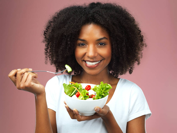 Fuel for the body. Studio shot of an attractive young woman eating salad against a pink background - Fotó, kép