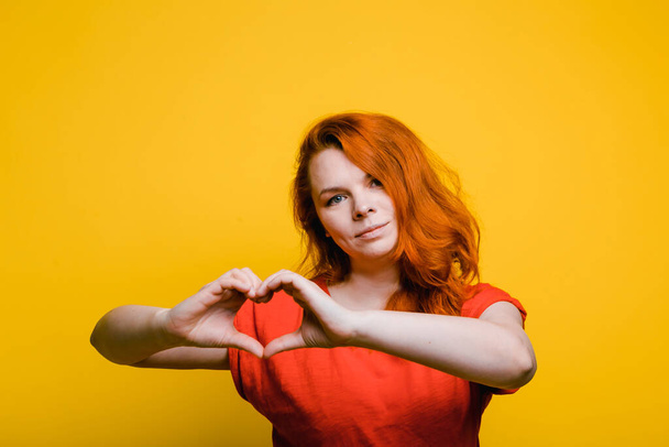 Genç kırmızı harmed kadın kalp hareketi gösteriyor, parlak sarı arkaplan - Fotoğraf, Görsel