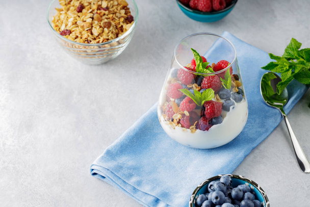 Healthy breakfast in glass of parfait. Yogurt with granola and berries on a blue napkin. Fresh raspberries and blueberries with homemade granola and yogurt - Foto, Imagem