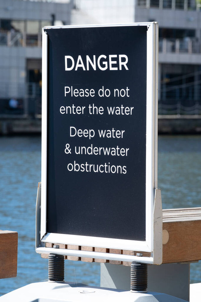 Warnschild zur Benachrichtigung der Öffentlichkeit, sich in der Nähe des Kais aufzuhalten, aufgrund der tiefen Wasser- und Unterwasserhindernisse an der Canary Wharf, London. - Foto, Bild