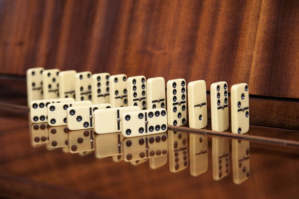 Τα στοιχεία του επιτραπέζιου ντόμινο παιχνίδι βρίσκονται, στέκεται τοποθετημένα σε ένα ξύλινο φόντο. Ένα ενδιαφέρον επιτραπέζιο παιχνίδι ντόμινο για όλη την οικογένεια - Φωτογραφία, εικόνα