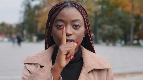 Close-up young confident mysterious african american woman standing outdoors showing silence gesture puts finger to mouth forbids speaking prohibits disclosure confidential information secret concept - Video