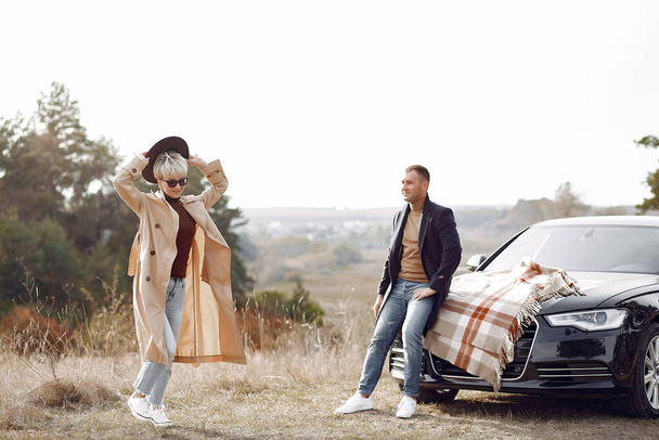 Couple in a field. Girl in a brown coat. Man with his wife near the car - Fotó, kép