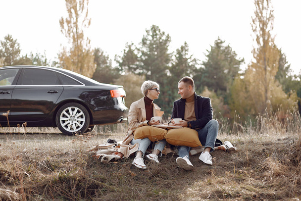 Couple in a field. Girl in a brown coat. Man with his wife near the car - Foto, immagini