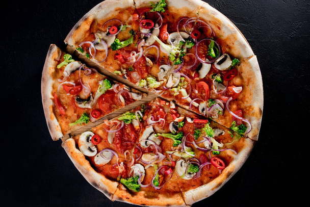 Vegan pizza with tomato sauce, cherry tomatoes, mushrooms, broccoli, red onion on black background. View from above. - Photo, Image