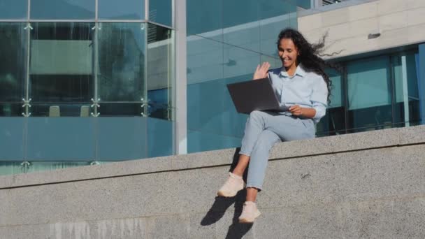 Jovem mulher de negócios estudante sentada na rua cidade edifício empresa de fundo com laptop fazendo videochamada conferência on-line bate-papo acenando Olá conversação remota falando negociação - Filmagem, Vídeo