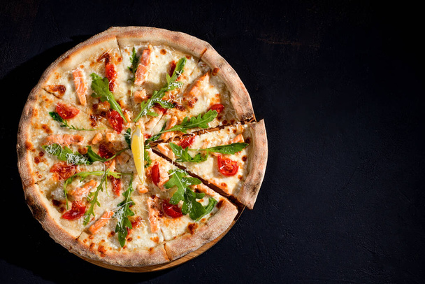 Pizza with salmon, mozzarella, cherry tomatoes, arugula, lemon and parmesan. Italian cuisine. On a black background. Free space for text. View from above - Valokuva, kuva