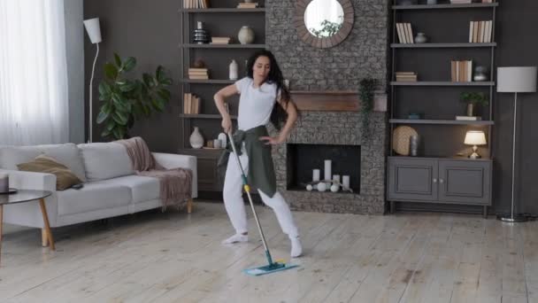 Ενεργειακά ευτυχισμένη νεαρή γυναίκα νοικοκυρά σφουγγαρίζοντας πάτωμα στο σαλόνι εκτελεί χορογραφικές κινήσεις ενεργό ελκυστικό κορίτσι χορεύοντας μουσική, ενώ ο καθαρισμός σπίτι πλένει διαμέρισμα απολαμβάνοντας νοικοκυριό - Πλάνα, βίντεο