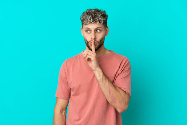Junge schöne kaukasische Mann isoliert auf blauem Hintergrund zeigt ein Zeichen des Schweigens Geste legt den Finger in den Mund - Foto, Bild