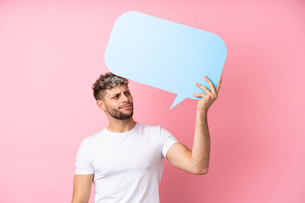 Young handsome caucasian man isolated on pink background holding an empty speech bubble - Фото, зображення