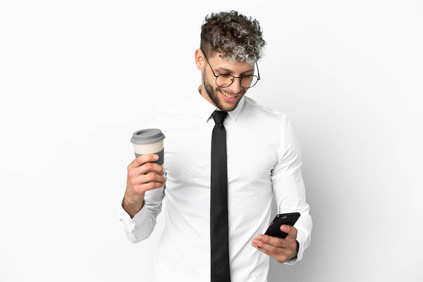 Business caucasian man isolated on white background holding coffee to take away and a mobile - Фото, изображение