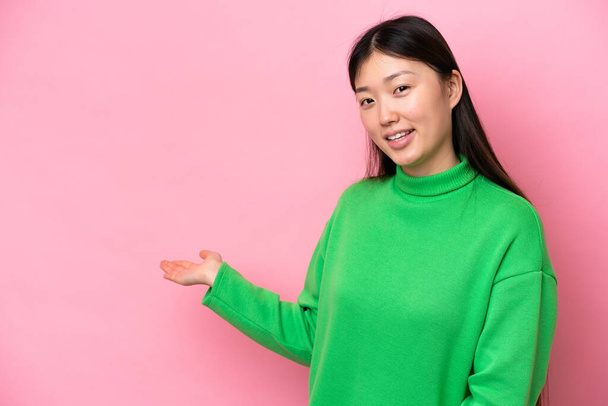 Young Chinese woman isolated on pink background extending hands to the side for inviting to come - Foto, Imagem