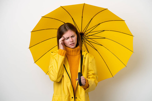 Молода англійська жінка з дощовитим пальто і парасолька ізольована на білому тлі з головним болем. - Фото, зображення