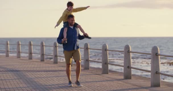 Father and son bonding, playing and having fun on the beach as a family by the sea in summer. Dad carrying his boy child on his shoulders, walking and enjoying a day out by the ocean on vacation. - Πλάνα, βίντεο