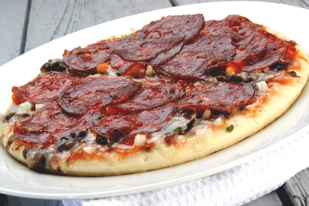 Острая пицца с салями на белой тарелке
 - Фото, изображение
