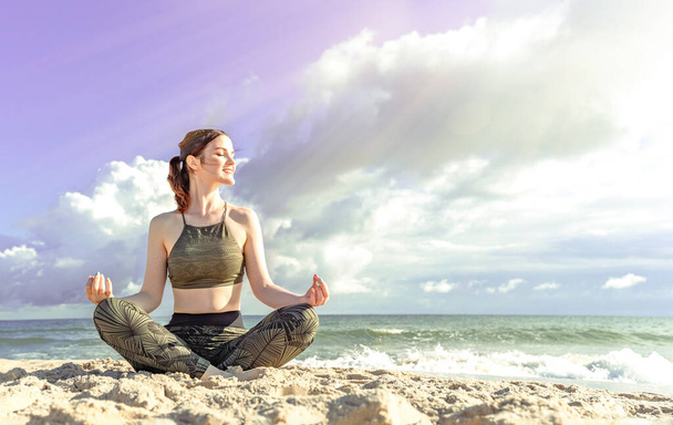 Woman in lotus position on beach. Girl enjoys meditation outdoors. Yoga harmony of soul and body healing - 写真・画像
