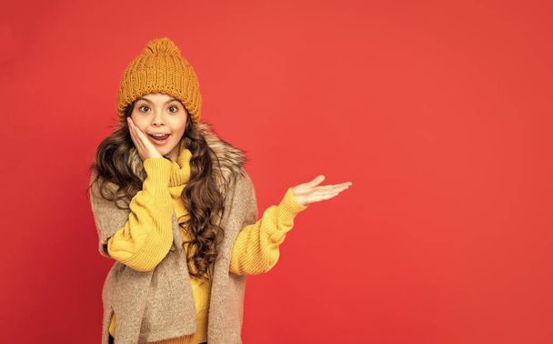 έκθαμβος παιδί σε πλεκτό καπέλο χειμώνα παρουσιάζοντας το προϊόν στο χώρο αντίγραφο, διαφήμιση. - Φωτογραφία, εικόνα