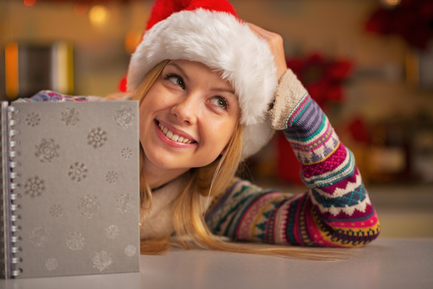 Portrait of thoughtful teenager girl in santa hat with notepad - Photo, image