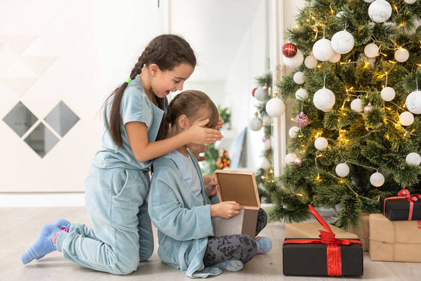 Two cute little girls under Christmas tree. Children under Christmas tree with gift boxes. New Years decorations. Sisters. - Photo, Image