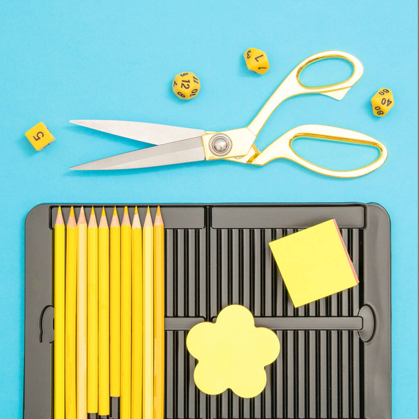 Top view composition of yellow pencils,  post it notes, polyhedral dices and scissors over turquoise blue background. Flat lay. Creativity, workspace, back to School concept. - Foto, afbeelding
