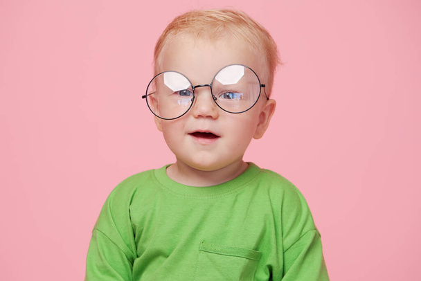 Portrait of male baby boy on pink background wearing glasses and looking at the camera. Smart baby concept - Фото, зображення