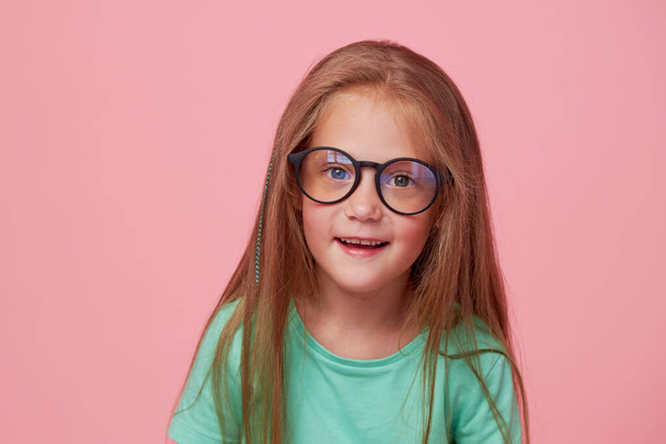 Portrait of cute toddler girl child bespectacled over pink background. Advertising childrens products. Funny face - Fotó, kép