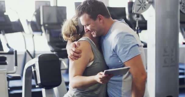 Personal trainer or coach talks to a client about goals and exercise schedule on a tablet. Real plus size fitness instructor consulting active normal man about workout performance at the gym. - Video