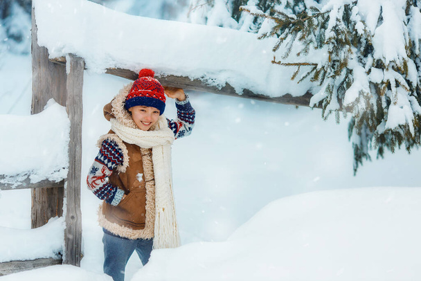 Happy child boy on a winter walk outdoors smiling and looking at camera. Kid is wearing red hat and white scarf. Kid is having fun, playing at winter walk outdoors. - Foto, Imagen