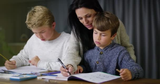 Mother helping boys with homework assignment, teaching and learning. Homeschool son and little brother learning education with a friendly and caring female tutor, smiling and tutoring smart children. - Video, Çekim