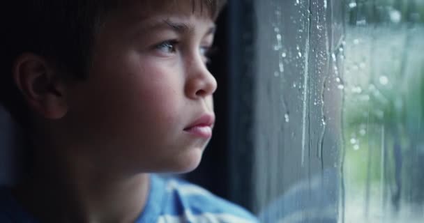Грустный маленький мальчик с психическими проблемами, смотрящий в одиночестве и скучающий, глядя на дождь из окна. ПТСР, насилие и травма жертвы застряли в плохой, токсичной среде. Сирота чувствует себя одиноким и подавленным. - Кадры, видео